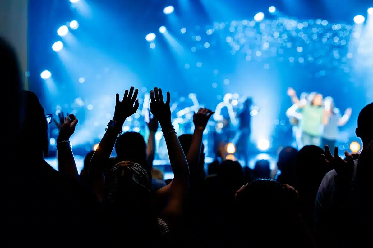 Silhouetted musicians perform on stage with dramatic concert lighting and crowd in background