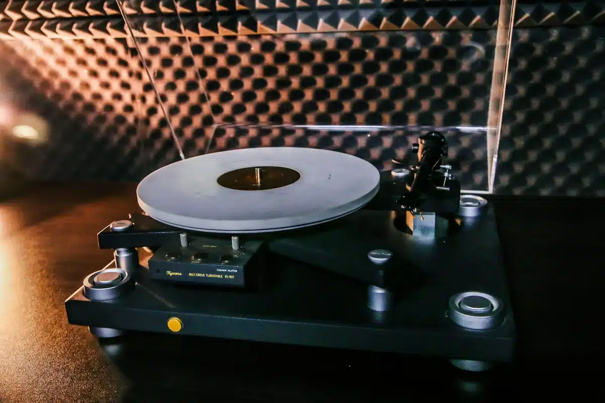 Hands holding an acoustic guitar and vinyl record in warm lamplight in a home studio setting