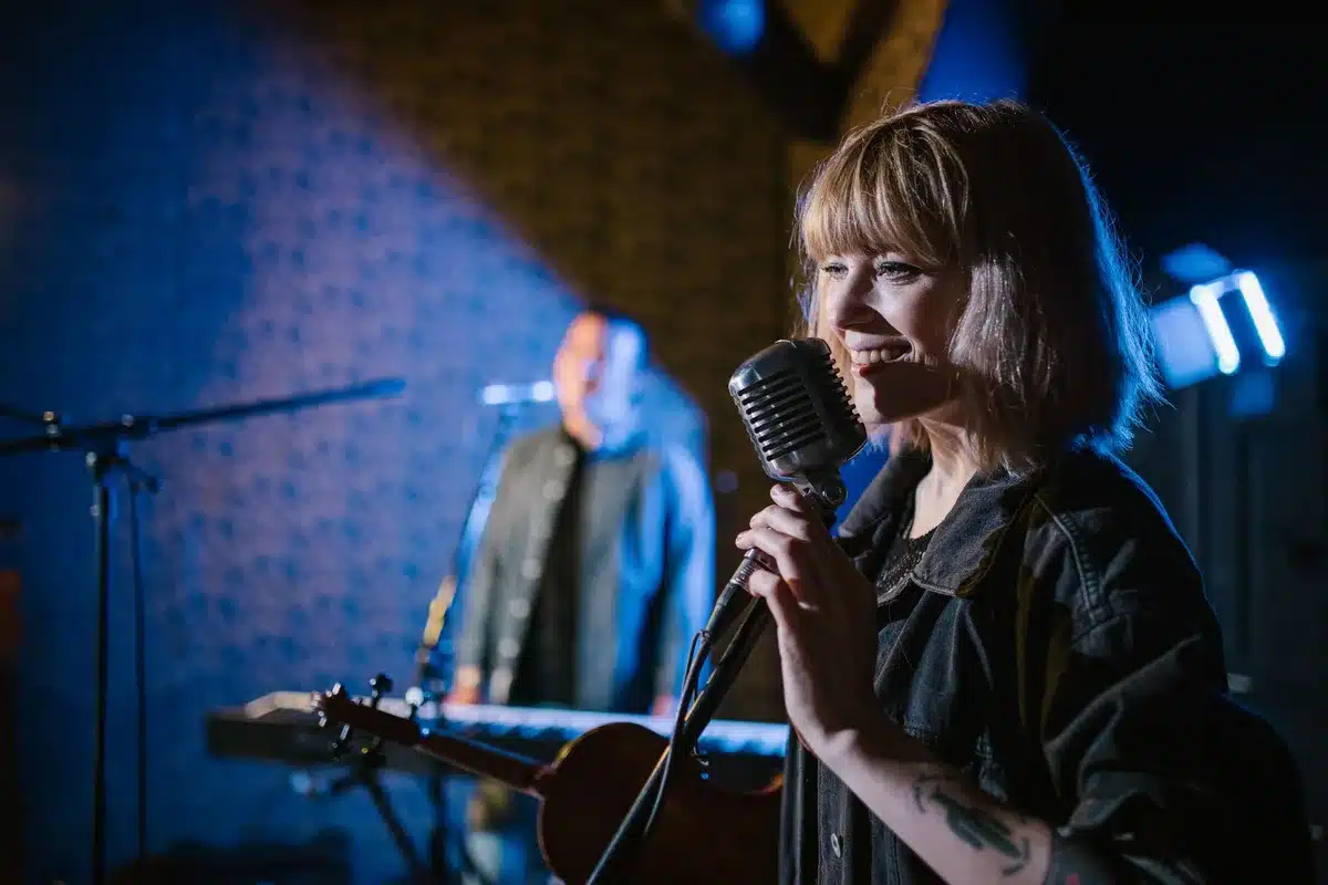 Artist performing with acoustic guitar and subtle piano accompaniment on stage