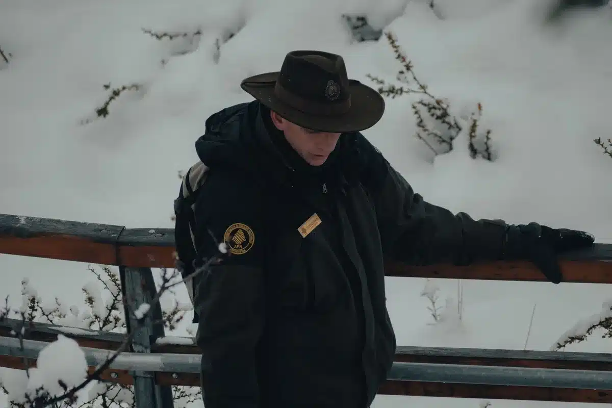 Park ranger standing on a hiking trail near a posted rules sign