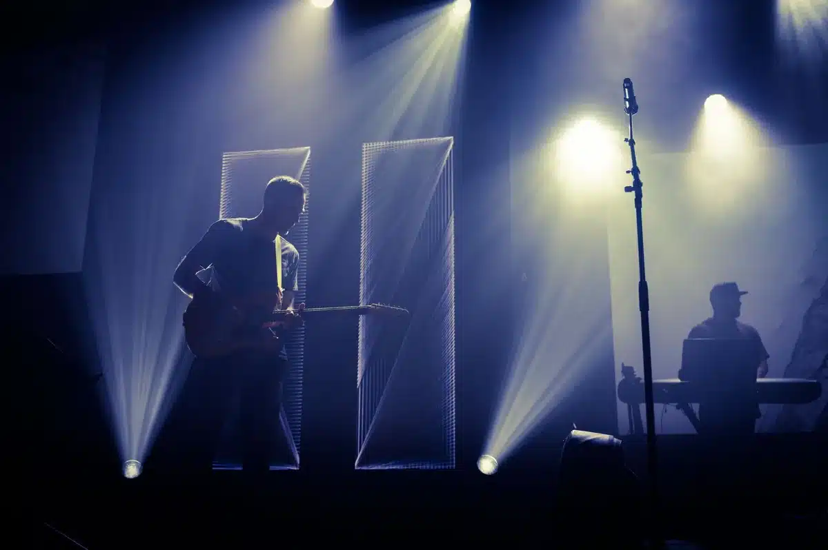 Una banda en vivo bajo iluminación tenue en un gimnasio, con efectos de grano y contrastes oscuros típicos de la estétic