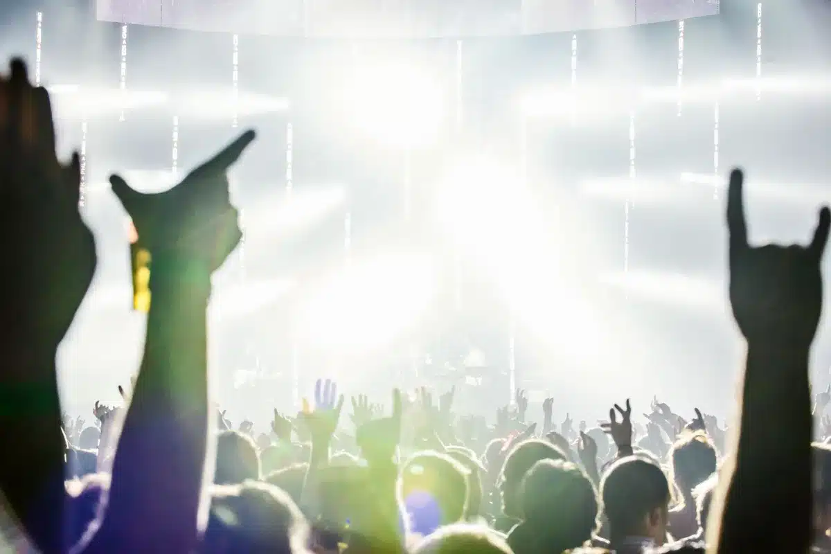 Crowd of college students at outdoor house party with raised phones and stage lights