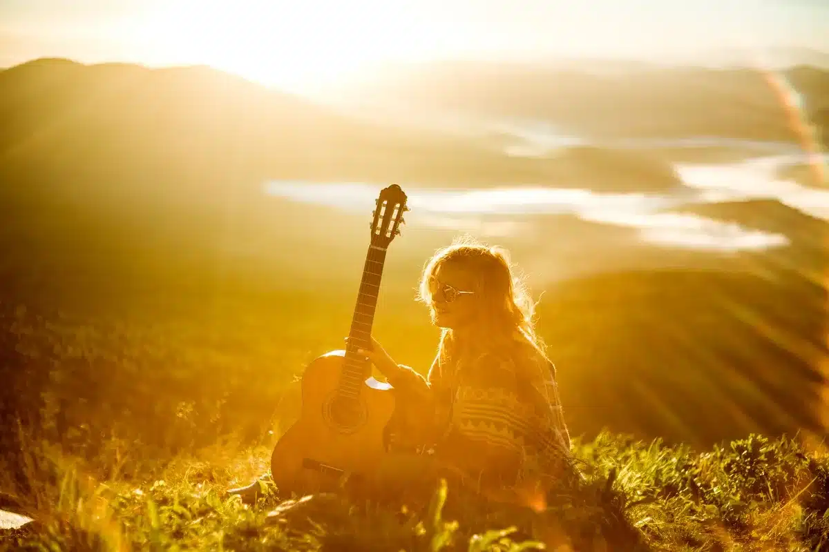 Musician with guitar silhouetted against golden sunset over ocean water