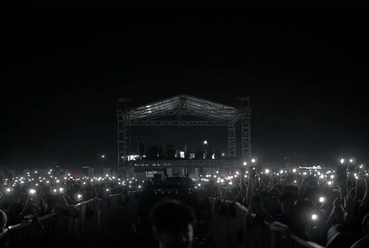 Concert stage with silhouetted performer and crowd recording on phones under stage lights