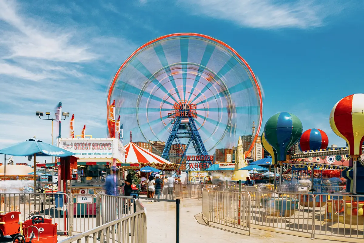 Vibrantly lit state fair midway with rides, food stalls, and crowds of visitors enjoying the carnival atmosphere.