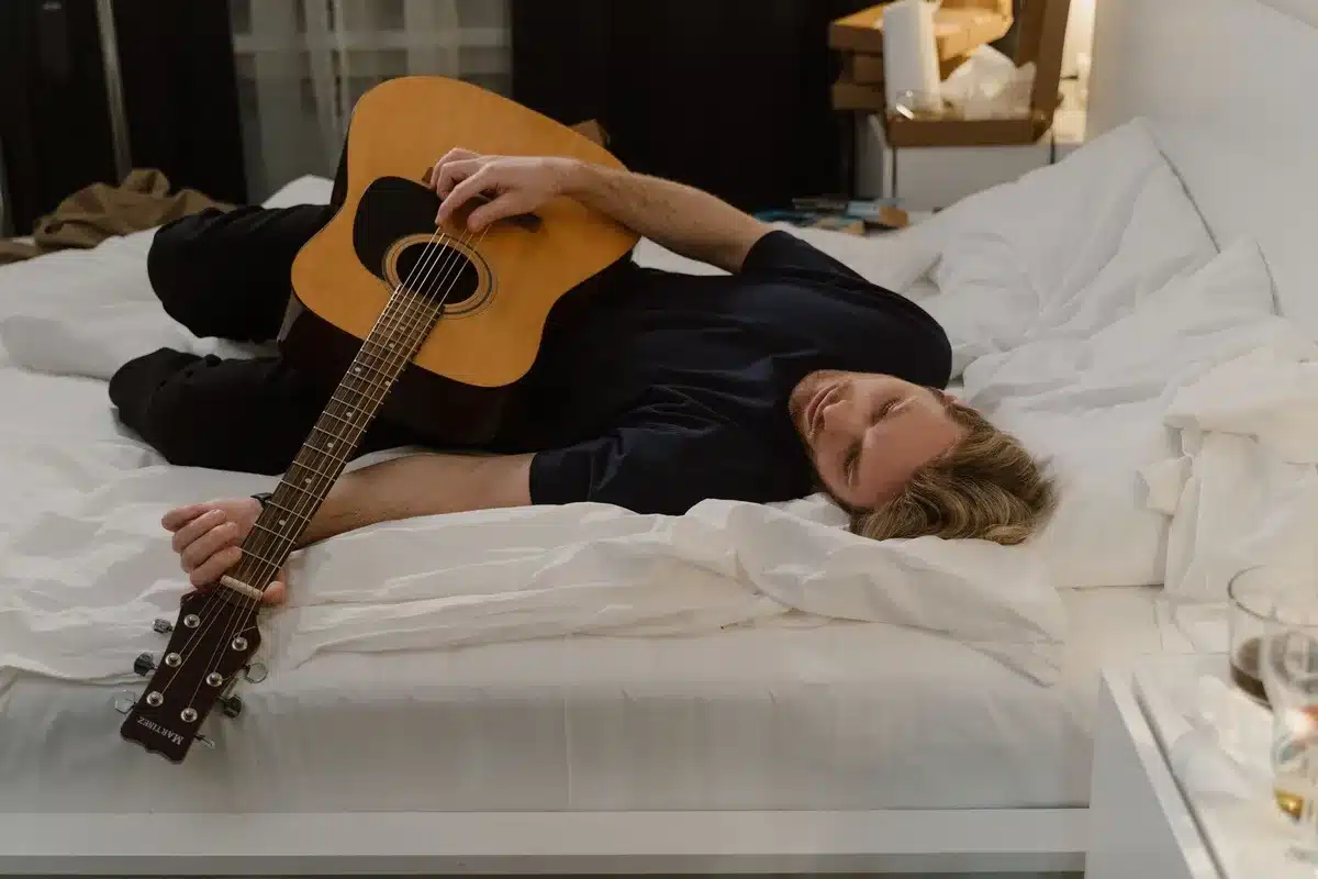 Eine Gitarre liegt auf einem Bett in einem dunklen Zimmer, das Gefühl von Einsamkeit und Isolation vermittelnd.