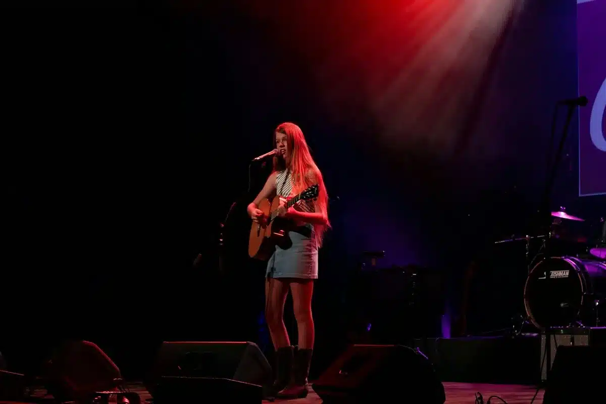 A young female performer on stage with an acoustic guitar
