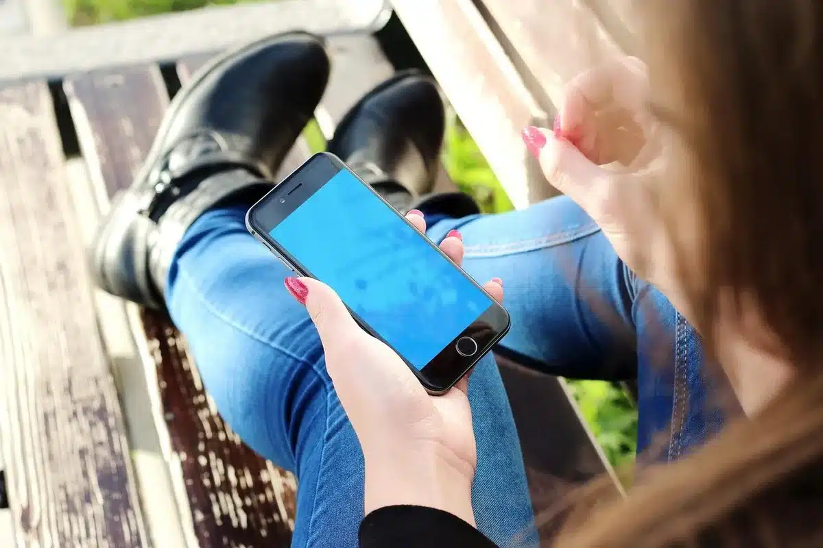 Hands holding a smartphone over a notebook and plant, blurred social feed visible