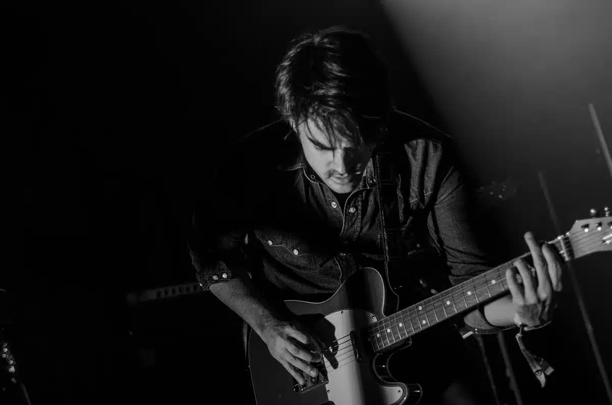 Musician with guitar and studio headphones recording atmospheric indie rock