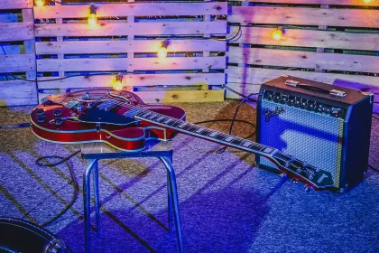 Hands on a worn guitar and vintage synth in a dim rehearsal room with neon reflection