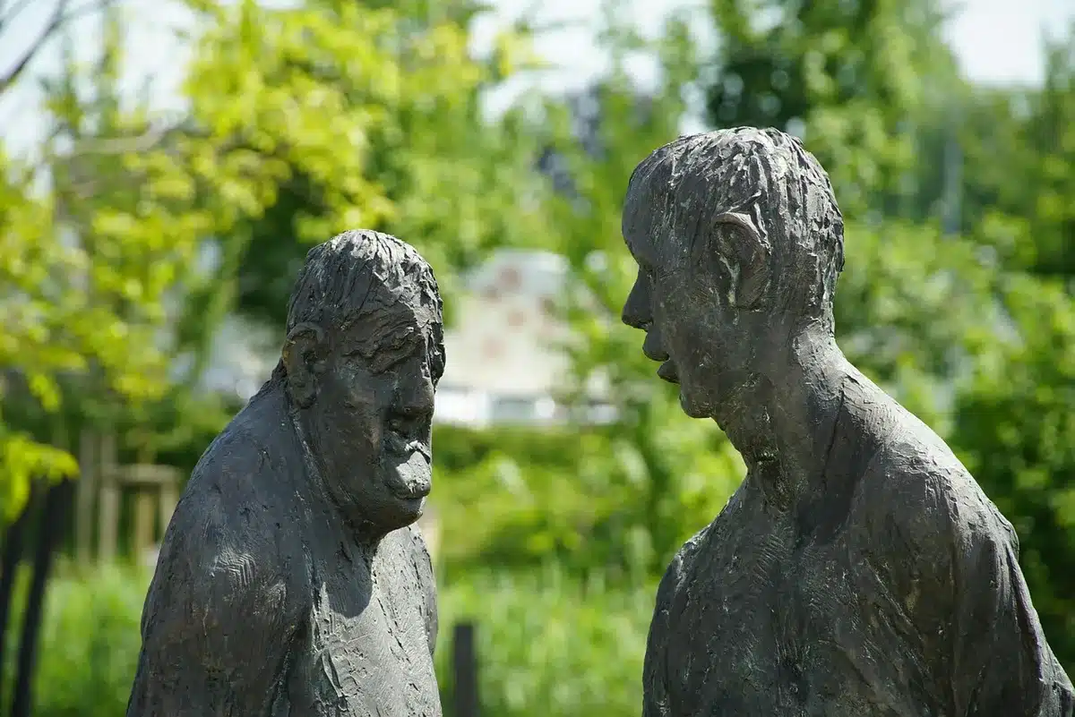 Two anonymous figures at a dim bar, one pausing mid-conversation