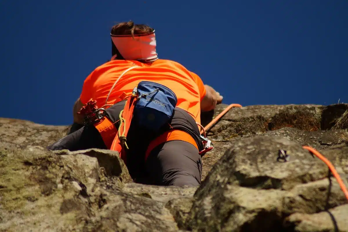 Climber pausing at a deadpoint on a rock face, hands stretched mid-reach