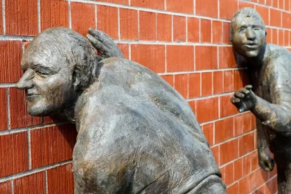 Bronze-style statue on a public plaza with anonymous onlookers taking photos