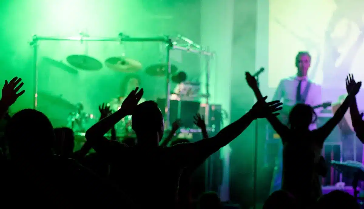 Enthusiastic crowd at a live music event with hands raised and lights overhead
