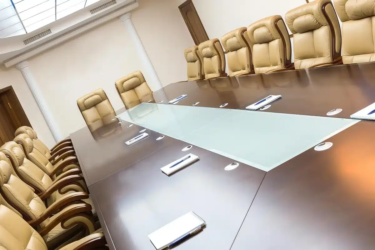 A formal board meeting table with documents and people in discussion about appointments