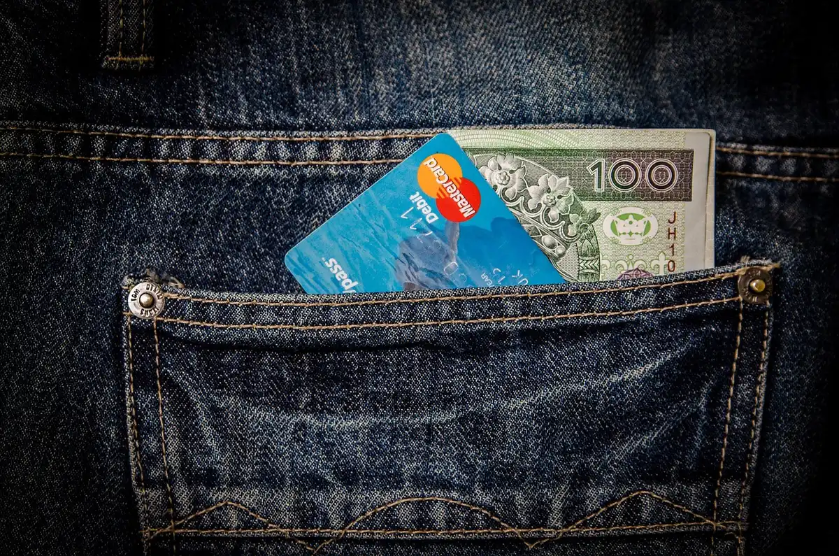 Hands holding novelty cards and a travel wallet on an airport security conveyor
