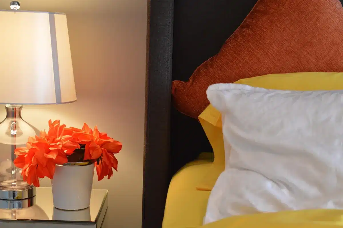 Dim bedside lamp with a phone showing a music player and a cup beside it