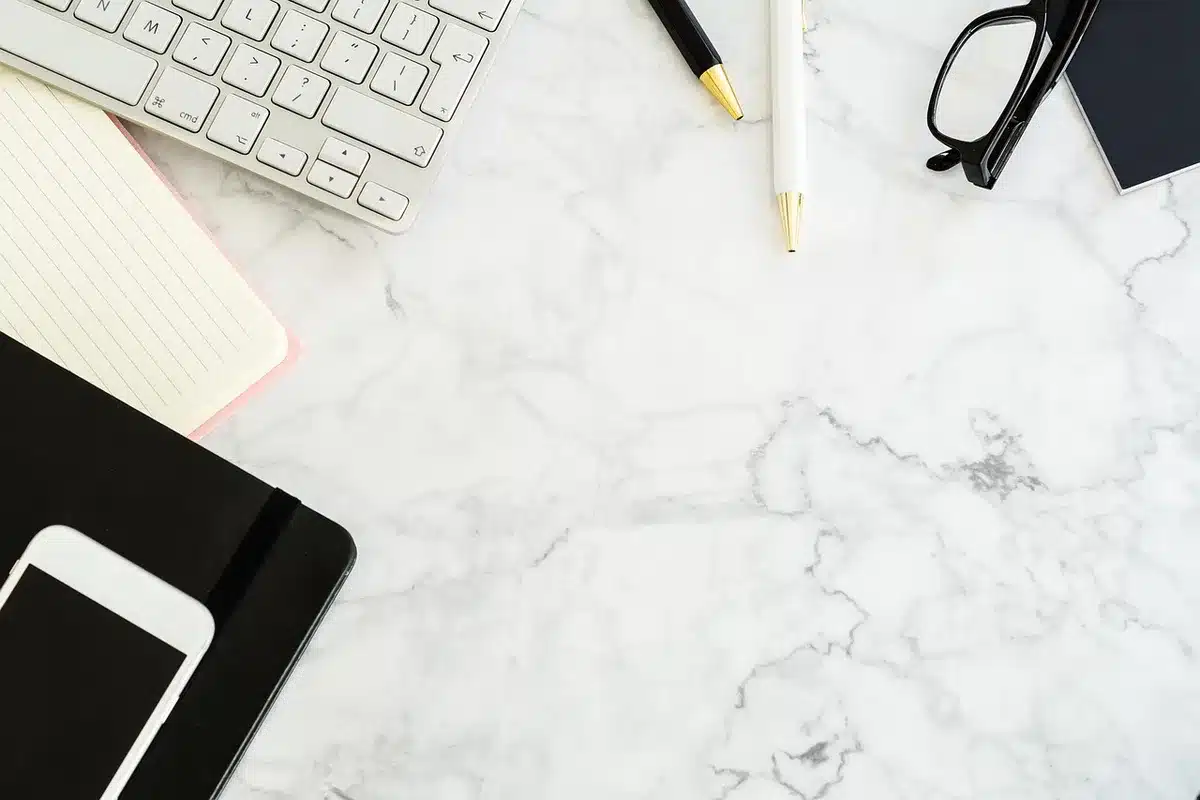 Hands scrolling a streaming playlist on a phone beside headphones and a notebook in a cafe