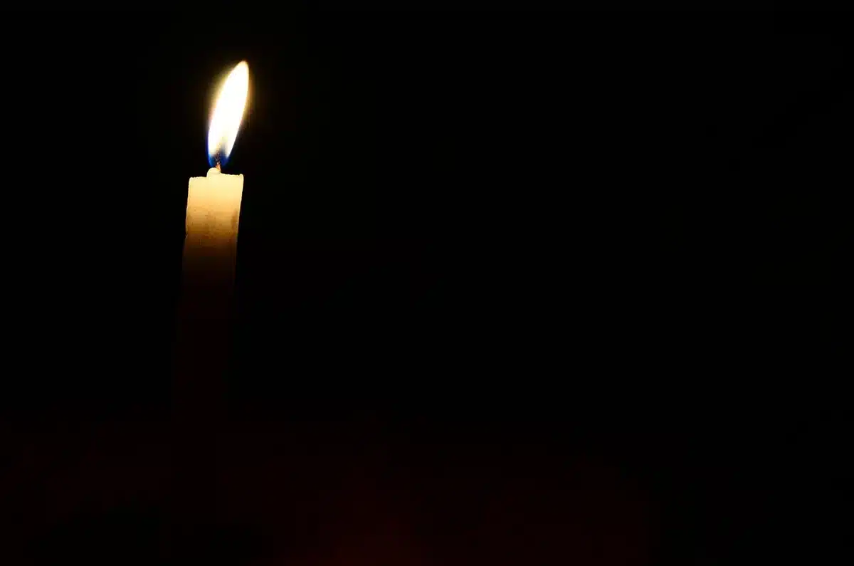 Hands holding lit candles and a note on a table in soft window light