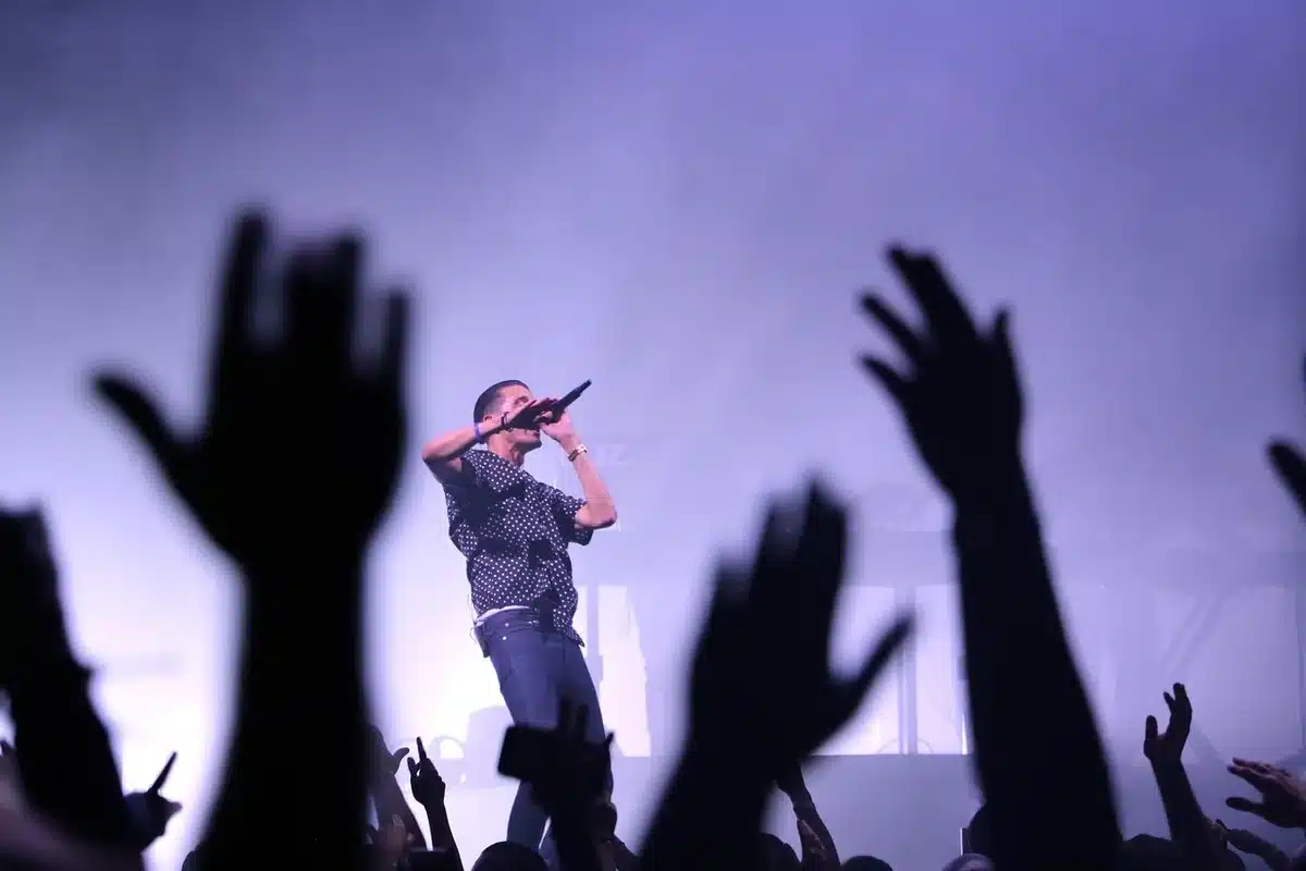 Silhouette of fan reaching microphone from crowd toward a low-lit stage