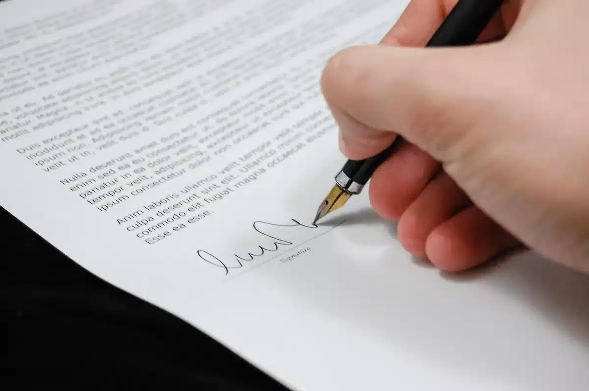 Hand signing legal documents on a desk with a pen