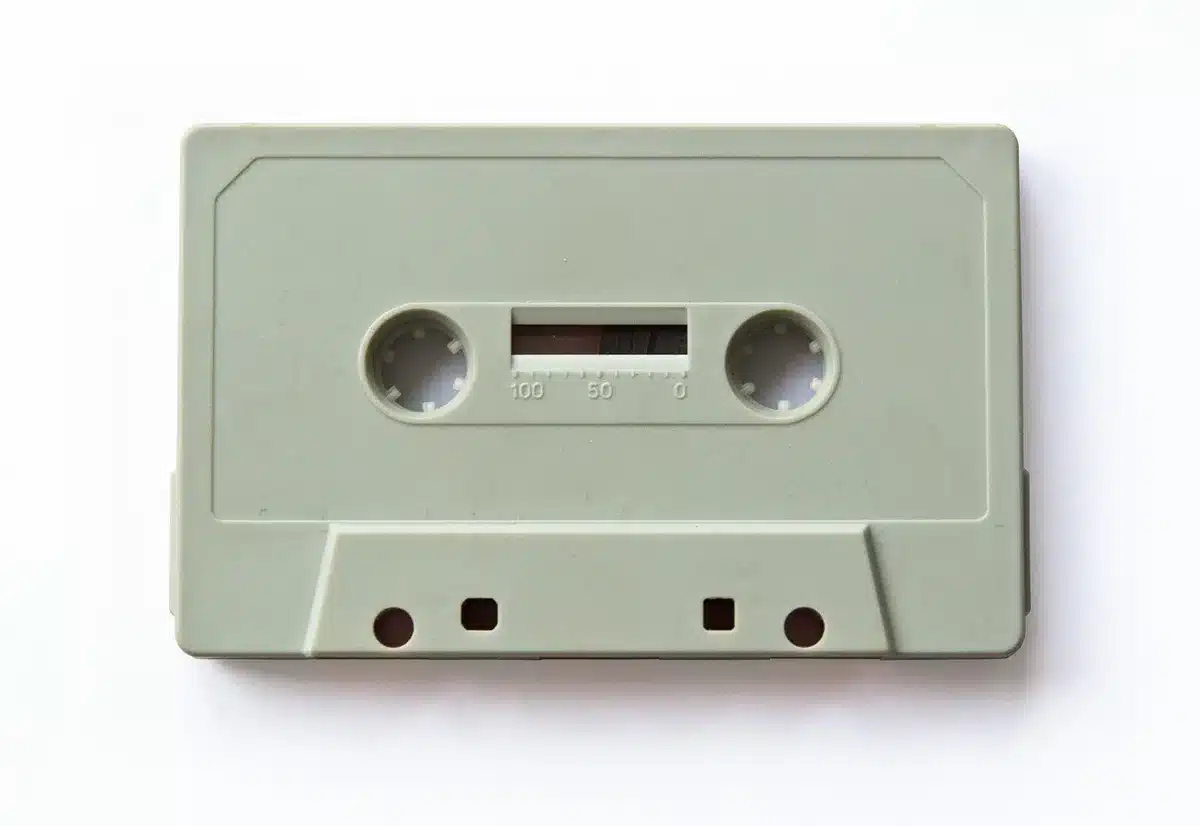 Hands holding a worn vinyl sleeve and cassette on a cluttered table
