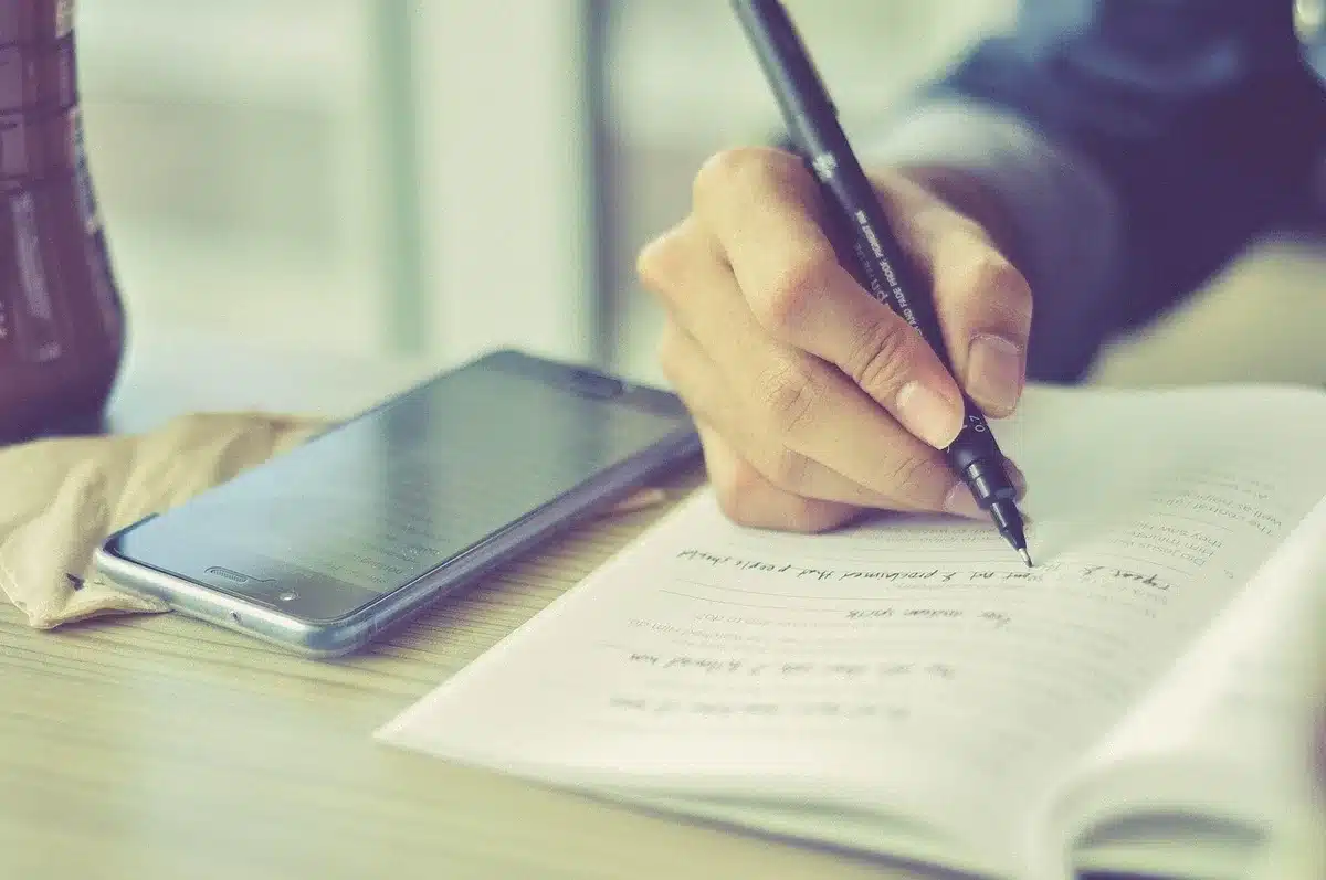 Hands with redacted documents and laptop on a conference table, newsroom figures blurred behind