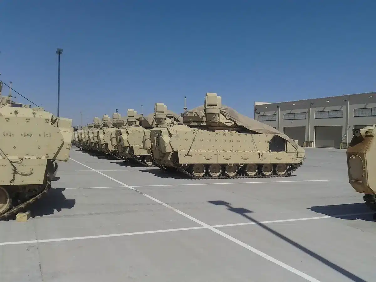 Unmarked vehicles parked near a fenced airbase perimeter under overcast sky