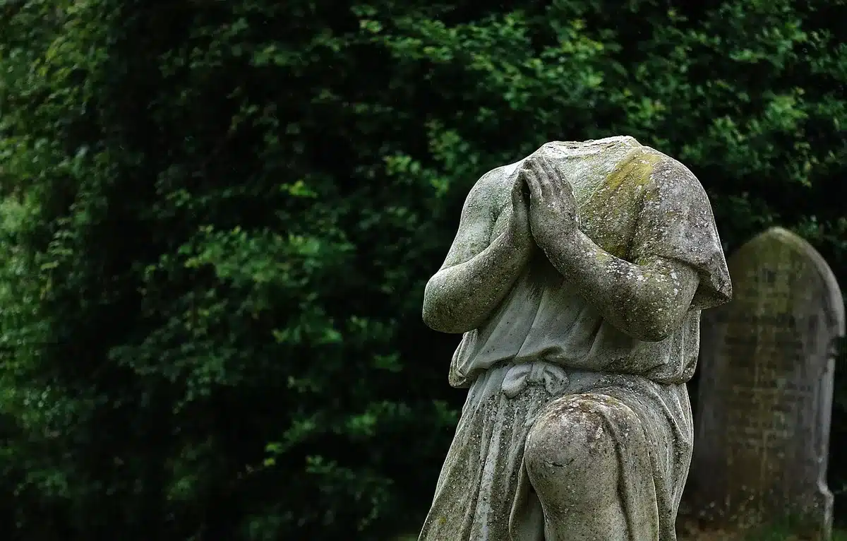 An anonymous hand places a folded scrap of paper at an old headstone in a shaded cemetery